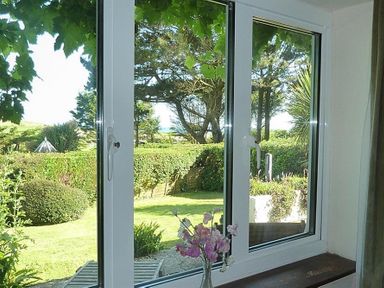 View of a garden with trees and bushes through a window with flowers on the sill at Willows in Charmouth