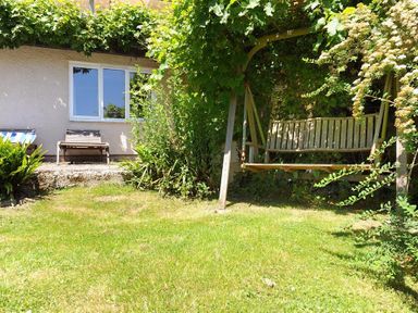 A garden with a wooden swing and two lounge chairs near a house at Willows in Charmouth
