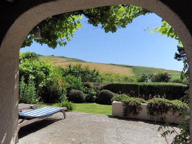 A garden with bushes and a lawn viewed through an archway at Willows in Charmouth