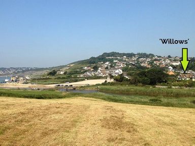 A view of a coastal village with houses on a hillside and a grassy field in the foreground at Willows in Charmouth