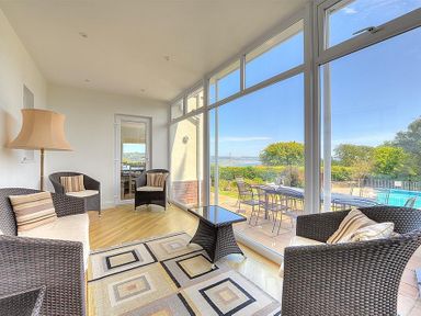 A sunroom with wicker chairs and a patterned rug overlooking a patio with a table and chairs at Somerhill in Lyme Regis