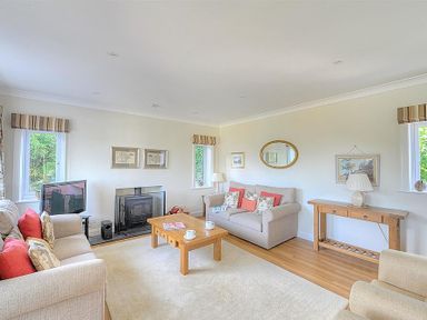 A living room with two beige sofas a wooden coffee table a wooden side table a fireplace and two windows at Somerhill in Lyme Regis