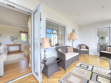 An enclosed patio with wicker chairs a table lamps and a rug next to a living room at Somerhill in Lyme Regis