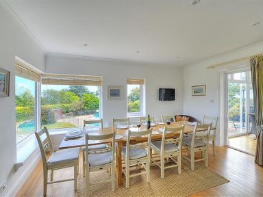 A dining room with a wooden table and chairs next to large windows and glass doors at Somerhill in Lyme Regis