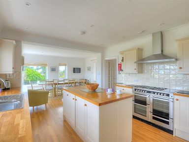 A kitchen with an island, a stainless steel stove, wooden counters, and a dining area with chairs and a table at Somerhill Lyme Regis