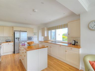A kitchen with wooden countertops a kitchen island a refrigerator and a window with a striped blind at Somerhill in Lyme Regis