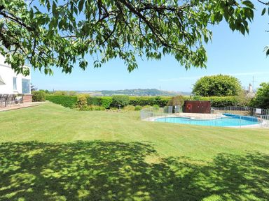 A grassy garden with a fenced swimming pool and patio furniture outside a house at Somerhill in Lyme Regis