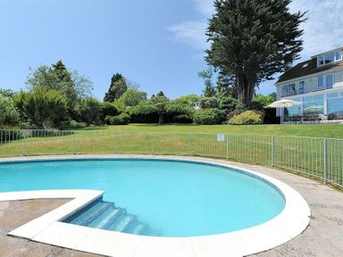 A swimming pool with steps leading into it in a garden with grass and trees near a house at Somerhill in Lyme Regis