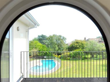 A view of a backyard with a swimming pool and trees seen through an arched balcony railing at Somerhill in Lyme Regis