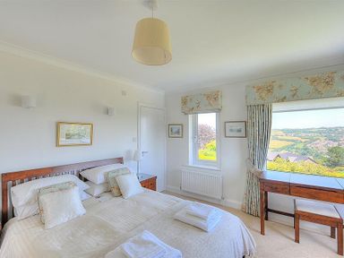 A bedroom with a double bed pillows folded towels a wooden desk and chair and a window with a view at Somerhill in Lyme Regis
