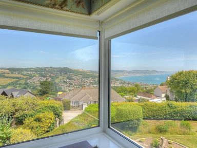 A view of a coastal town and hillside seen through corner windows at Somerhill in Lyme Regis