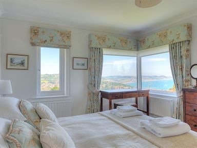 A bedroom with a bed desk chair windows with curtains and a view of the sea at Somerhill in Lyme Regis