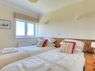 A bedroom with two single beds with pillows and folded towels by a window at Somerhill in Lyme Regis