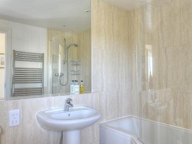 A bathroom with a white pedestal sink, a bathtub with a glass shower screen, a wall-mounted showerhead, and a chrome towel radiator at Somerhill in Lyme Regis