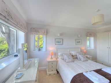 A bedroom with a bed pillows bedside tables lamps a dresser with mirror and three windows at Somerhill Lyme Regis