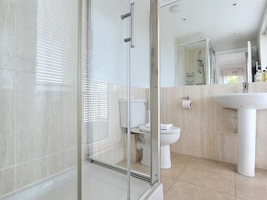 A bathroom with a glass shower enclosure a toilet and a pedestal sink with toiletries at Somerhill Lyme Regis