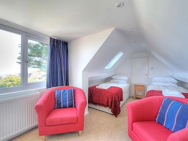 A bedroom with two single beds two red armchairs blue curtains and a small wooden nightstand at Somerhill in Lyme Regis