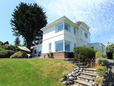 A white two-story house with large windows a stone staircase leading to the garden and outdoor patio furniture with umbrella at Somerhill in Lyme Regis