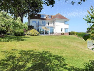 A large white house with multiple windows and a balcony surrounded by a grassy lawn and trees at Somerhill in Lyme Regis