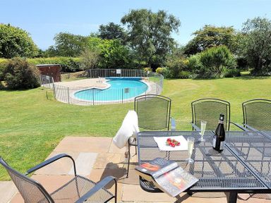A patio table with books and drinks overlooking a fenced swimming pool and garden at Somerhill in Lyme Regis