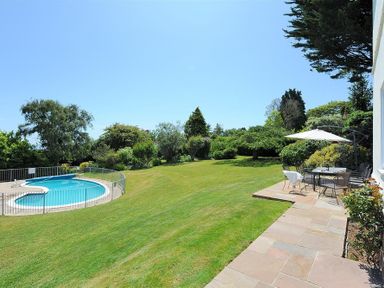 A garden with a swimming pool and outdoor dining area with umbrella at Somerhill in Lyme Regis