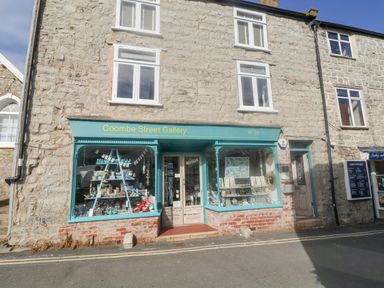 Stone building with two upper windows and a gallery shop with turquoise window frames and door at Coombe Street Gallery in Lyme Regis