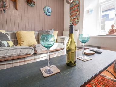 A living room with blue wine glasses on a table and a sofa behind at Coombe Street Cottage in Lyme Regis