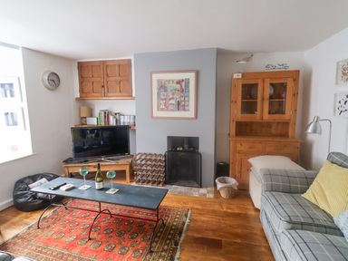 A living room with a sofa a coffee table wine glasses a TV and a wooden cabinet at Coombe Street Cottage Lyme Regis