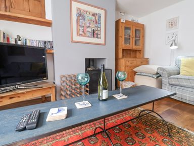 A living room with a black coffee table holding wine glasses and bottle in front of a fireplace and a plaid sofa at Coombe Street Cottage Lyme Regis