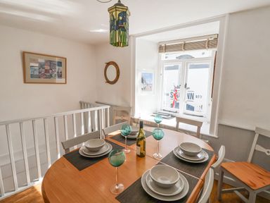 A dining area with a wooden table set for four near a window with chairs and wall decorations at Coombe Street Cottage Lyme Regis