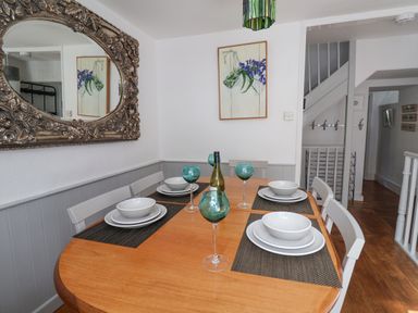 A dining area with a wooden table set with white dishes and blue glasses and an ornate mirror on the wall at Coombe Street Cottage in Lyme Regis