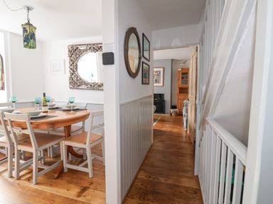A dining area with a wooden table and chairs and a hallway leading to a living room with wooden floors at Coombe Street Cottage in Lyme Regis