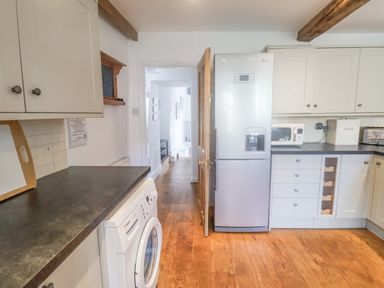 A kitchen with white cabinets a stainless steel fridge a washing machine and wooden floors at Coombe Street Cottage Lyme Regis