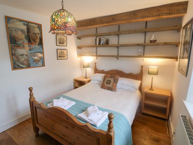 A bedroom with wooden bed and bedside tables with lamps and shelves on the wall at Coombe Street Cottage in Lyme Regis