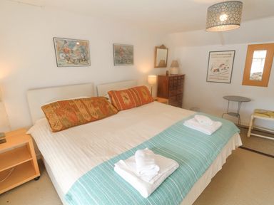 A bedroom with a large bed with cushions and towels bedside tables lamps and wall art at Coombe Street Cottage Lyme Regis