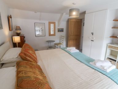A bedroom with a large bed two lamps a wooden door a white wardrobe and a small table with a chair at Coombe Street Cottage Lyme Regis