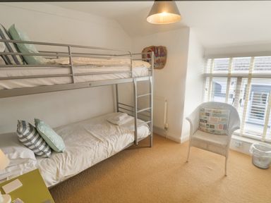 A bedroom with a metal bunk bed a chair with a pillow a window with blinds and a radiator at Coombe Street Cottage Lyme Regis