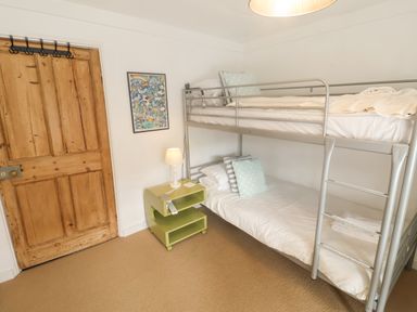 A bedroom with a metal bunk bed a wooden door a green bedside table and a lamp at Coombe Street Cottage Lyme Regis
