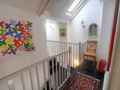 A hallway with a wooden chair a mirror a colorful flower painting a rug and a fire extinguisher at Coombe Street Cottage in Lyme Regis
