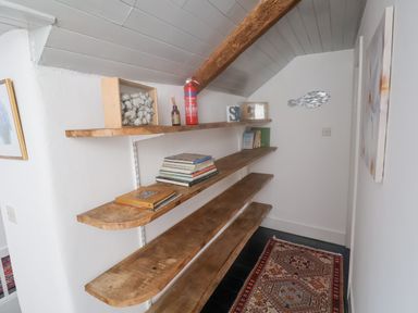 A narrow room with wooden shelves holding books and decorative items and a patterned rug on the floor at Coombe Street Cottage in Lyme Regis