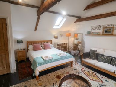 A bedroom with a double bed side tables a sofa a floor mirror and exposed wooden beams at Coombe Street Cottage in Lyme Regis
