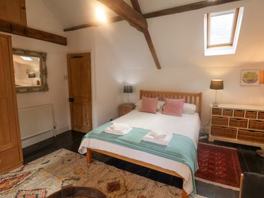 A bedroom with a double bed two pink pillows two lamps a wicker drawer unit and a skylight window at Coombe Street Cottage in Lyme Regis