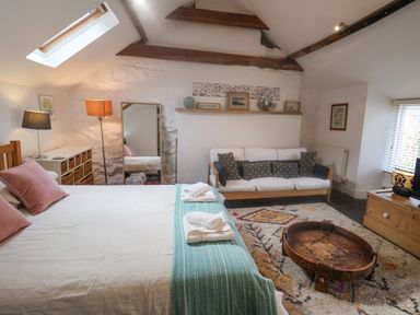 A bedroom with a bed towels a sofa a wooden coffee table a dresser and exposed wooden beams at Coombe Street Cottage in Lyme Regis