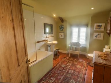A bathroom with a bathtub sink toilet wicker chair rug and wooden cabinet at Coombe Street Cottage Lyme Regis