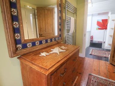 A wooden chest of drawers with starfish decorations a mirror with decorative tiles a hallway with rugs and a radiator at Coombe Street Cottage in Lyme Regis