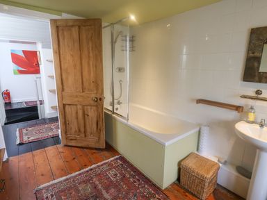A bathroom with a bathtub shower combination wooden door wicker basket and a sink at Coombe Street Cottage in Lyme Regis