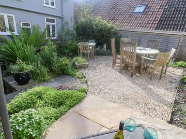 A garden with wooden table and chairs on gravel surrounded by plants and a fence at Coombe Street Cottage in Lyme Regis