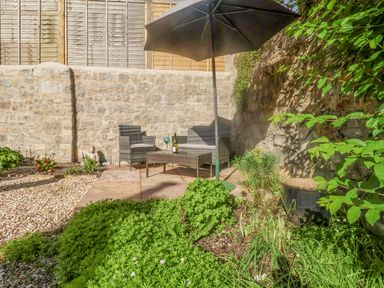 An outdoor patio with chairs a table a large umbrella stone walls and green plants at Coombe Street Cottage in Lyme Regis