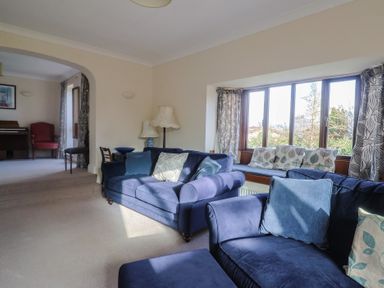 A living room with blue sofas and a piano at High Cliff Orchard in Lyme Regis