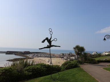 A view of a beach and marina with a sculpture at High Cliff Orchard in Lyme Regis